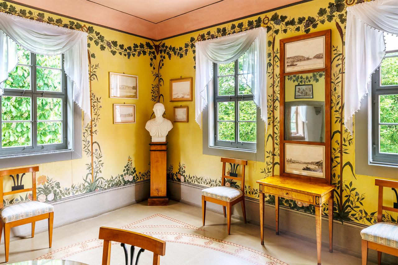 Ein Zimmer mit gelben Wänden und pflanzlichen Wandbemalungen im Schloss Tiefurt